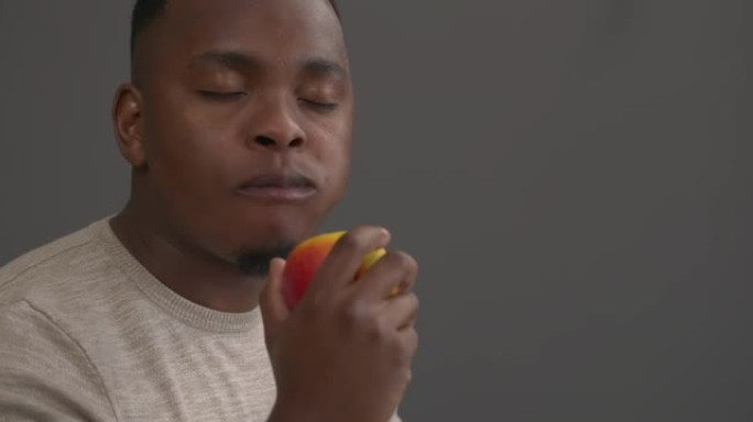 非洲男子食欲不振吃苹果的肖像。健康食品概念。孤立在灰色背景上