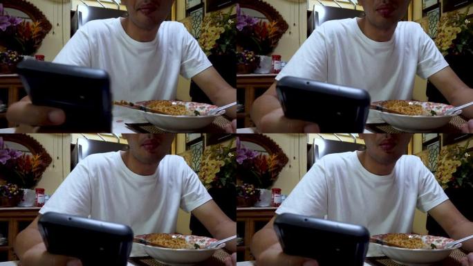 亚洲男子在使用智能手机时吃面。