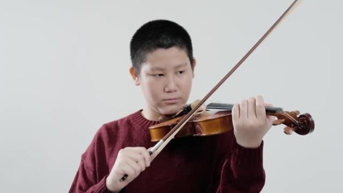 穿着毛衣的亚洲男生学习拉小提琴的灰色背景，生活方式的概念。