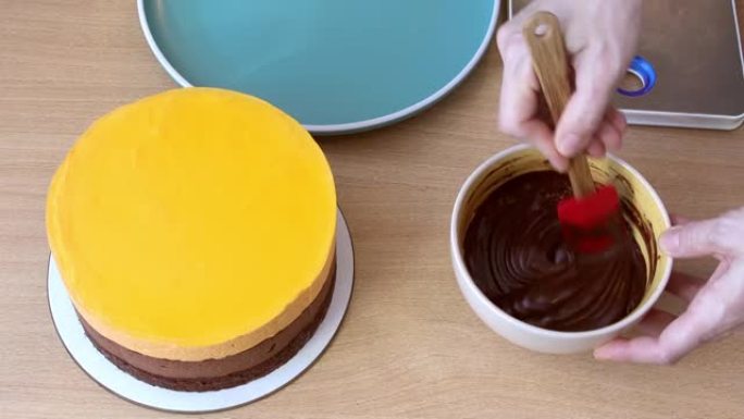 厨师将融化的黑巧克力与锅铲混合在碗中，用于蛋糕浇头