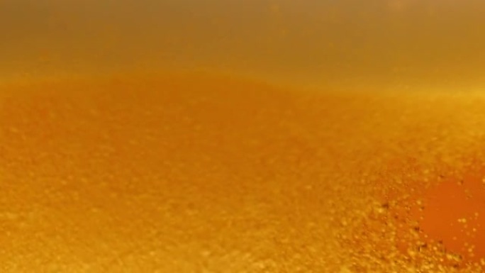 玻璃中轻啤酒微距。一小撮金色液体涌入玻璃，产生许多气泡、波浪和泡沫。新鲜酿造的酒精饮料啤酒特写。慢动
