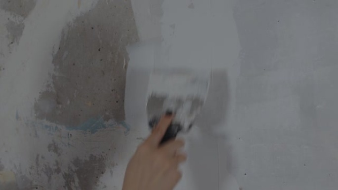 无法识别的人在房间的墙上涂油灰的特写。不知名的女人在公寓里用抹刀抹灰墙。维修工作和改善住房条件的概念