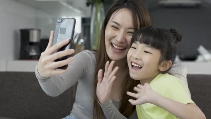 快乐的年轻亚洲妈妈和女儿用智能手机挥手和家人打招呼打视频电话。