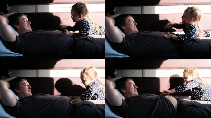 有趣的女孩孩子躺在微笑的父亲身上，打爸爸的肚子