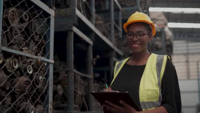 快乐的非洲裔美国工程师仓库工人的肖像，检查车库商店旧二手车发动机的清单清单。黑人妇女微笑着向汽车配件