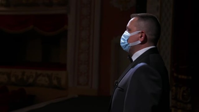 剧院演员戴着医用面具在舞台上讲话。穿着西装的播音员站在空荡荡的剧院大厅前。大流行概念。