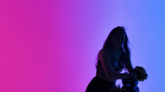 苗条的啦啦队长的剪影，在工作室里，在粉红色的蓝色灯光的背景下，手中的绒球充满活力地跳舞。体育比赛中的