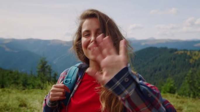 站在夏日群山中的女孩。微笑的女游客在镜头前挥手