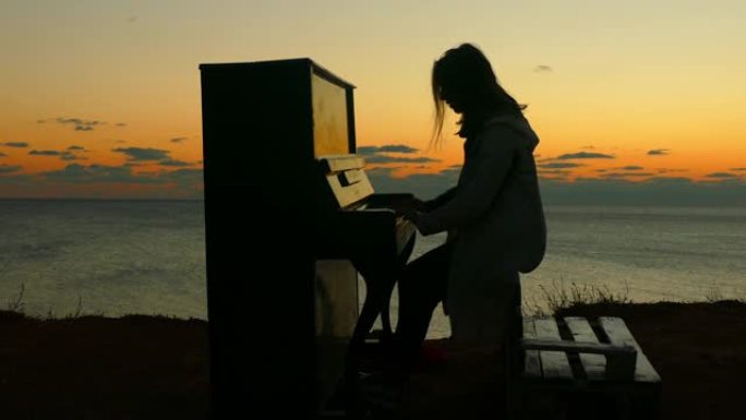 日落时在海岸上弹钢琴的女孩的剪影