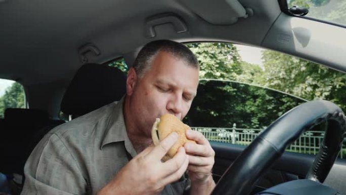 饥饿的男司机贪婪地在方向盘上吃汉堡