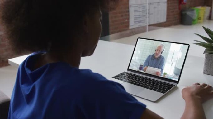 非裔美国妇女在办公室的笔记本电脑上与男同事进行视频通话的后视图