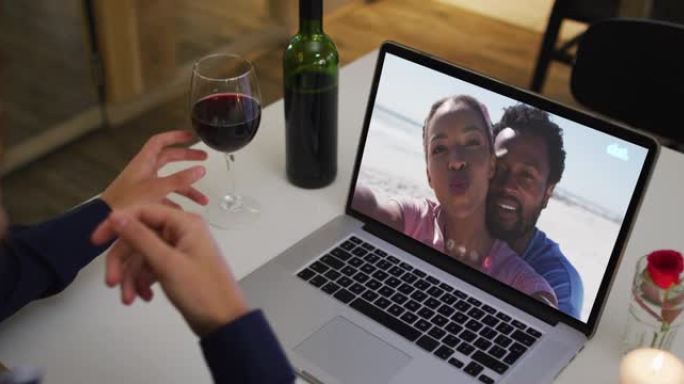 非洲裔美国妇女的中间部分拿着酒杯，同时在家里的笔记本电脑上进行视频通话