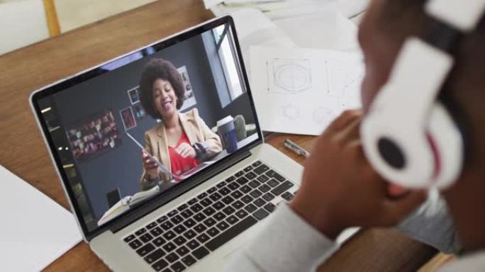 非裔美国商人坐在办公桌前，使用笔记本电脑与女同事进行视频通话