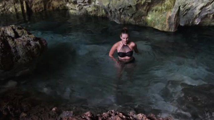 年轻女子在山洞的地下河中游泳，悬崖之间有淡水