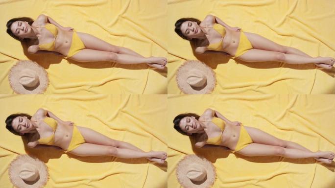 漂亮的女人躺在黄色棕褐色的毯子上洗日光浴