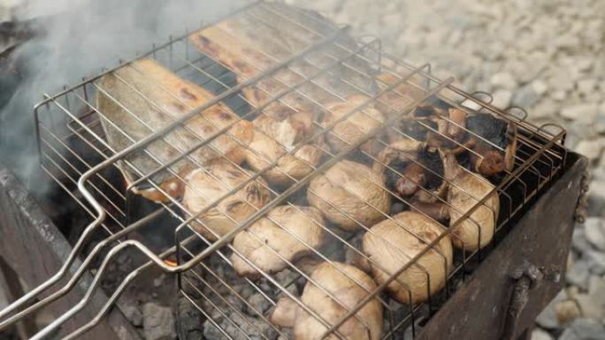 烤鱼和蘑菇烧烤。篝火。燃烧的木头。庭院夏季野餐。危险的烹饪