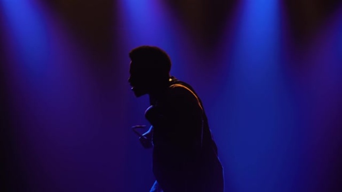 非洲民族音乐。一名非裔美国音乐家男子的剪影在一个黑暗的工作室里，在蓝色灯光的背景下，他在说话的非洲尤