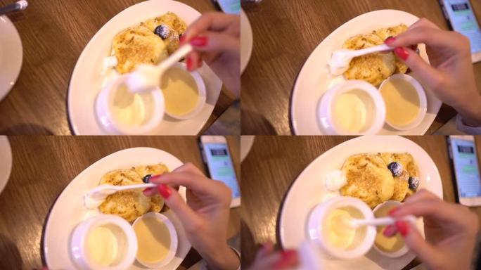 女人在咖啡馆吃甜点和喝咖啡，特写。女人把酸奶油放在油炸奶酪甜点里。在咖啡馆吃早餐的美女。4 k.女性