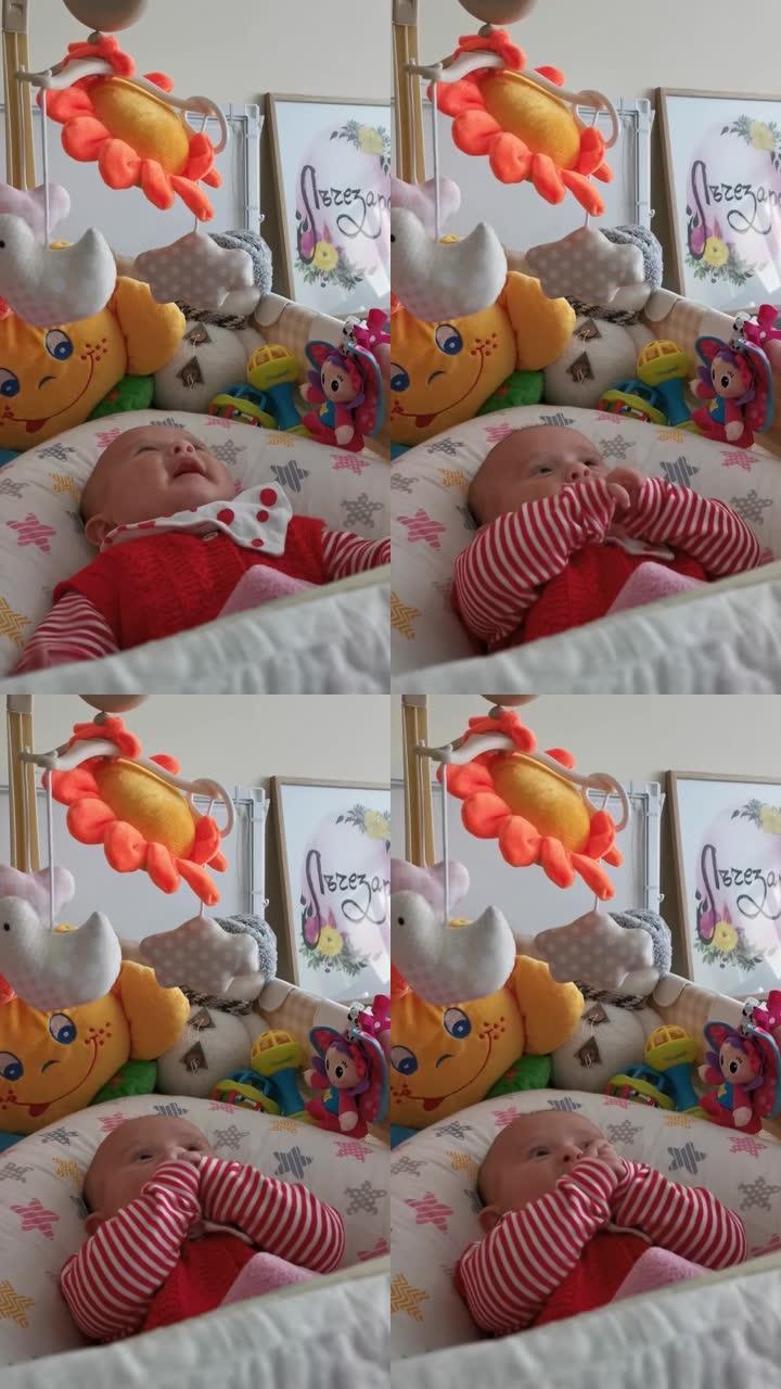 微笑的婴儿看着她的玩具，看着玩具旋转时笑着。三个月的女婴在床上玩耍。新型冠状病毒肺炎大流行期间的新生
