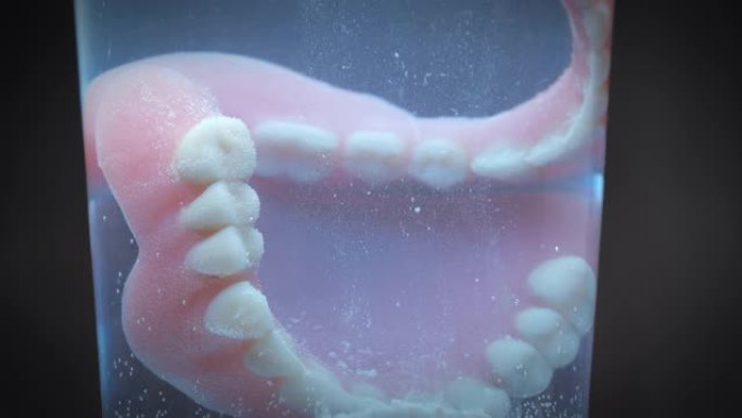 特写镜头显示假牙被装满清洗液的玻璃清洗。