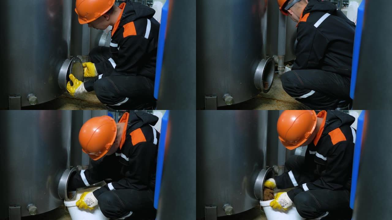 一名戴着头盔和手套的工人，取下舱口盖，以更换滤水箱中的滤芯。工业专业。危险的工作