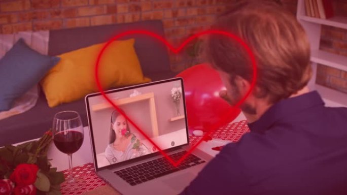 红色霓虹灯的心脏轮廓与白人男子在笔记本电脑上进行视频通话时挥舞着