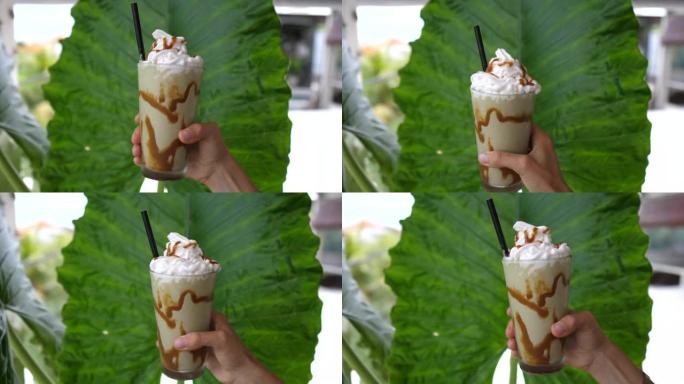 手在相机上展示了一杯冰抹茶绿茶，并在一块巨大的叶子的背景上放了鲜奶油