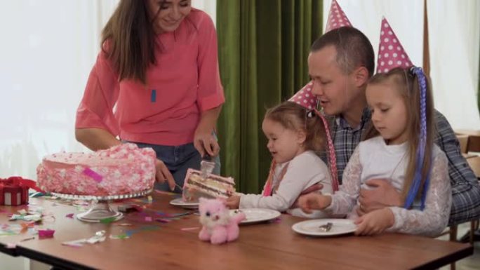 快乐的家庭举办派对。快乐的父母和孩子在室内庆祝生日。女儿端上盘子，妈妈端上蛋糕。