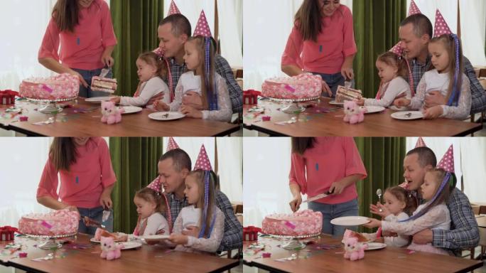 快乐的家庭举办派对。快乐的父母和孩子在室内庆祝生日。女儿端上盘子，妈妈端上蛋糕。