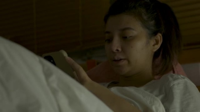 亚洲妇女在床上看电视和使用moblie的特写镜头。