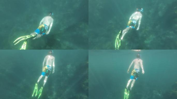 一个年轻的高加索人的水下视图，戴着带鳍和通气管的面具，在透明的海水中游泳。慢动作中的自由潜水