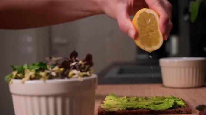 手榨柠檬汁在鳄梨上撒在面包上，健康饮食理念。