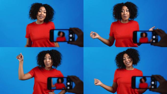 微笑的非洲博主女人制作了一个在线新视频博客，vlog与蓝色背景上的智能手机。有影响力的人在电话会议记