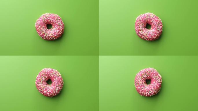 新鲜的甜甜甜圈覆盖着磨砂的粉红色巧克力亮洒旋转孤立在绿色上
