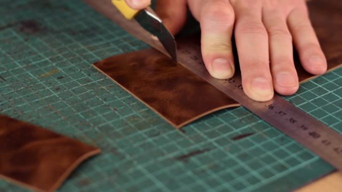坦纳用刀测量和切割皮革的手的特写。手工皮革制品的生产。爱好概念。慢动作。