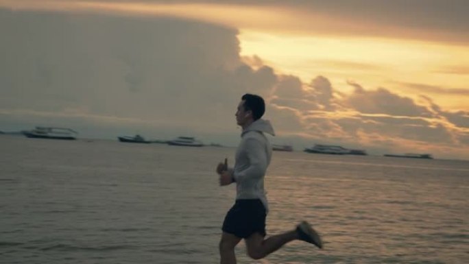 运动员年轻的亚洲人在海边奔跑，而美丽的日落在夏天。