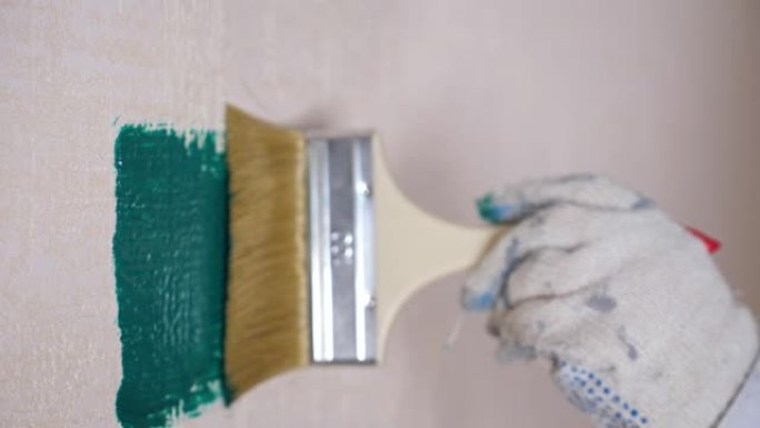 戴着脏手套的人把白色的墙漆成绿松石