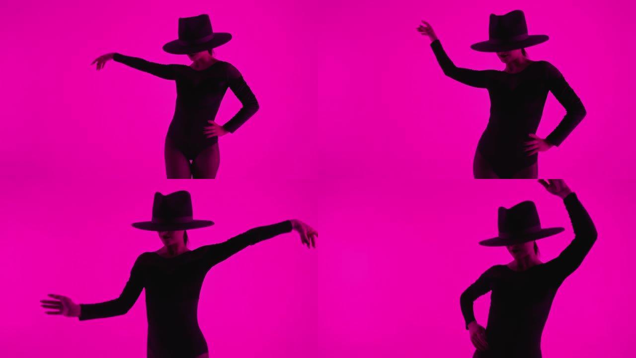 当代舞蹈家戴帽子的女人在彩色灯光下在粉色背景上摆姿势。职业芭蕾舞演员穿着性感的蛇蝎美人服装，独唱表演