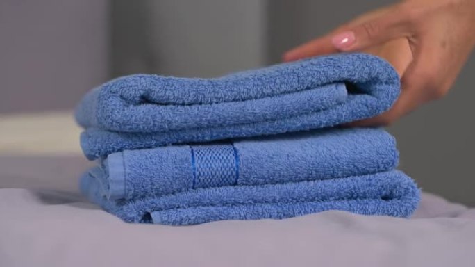 躺在床上的折叠浴巾特写。女人的手从堆栈中拿走一只。客房服务。家庭消遣概念。背景模糊