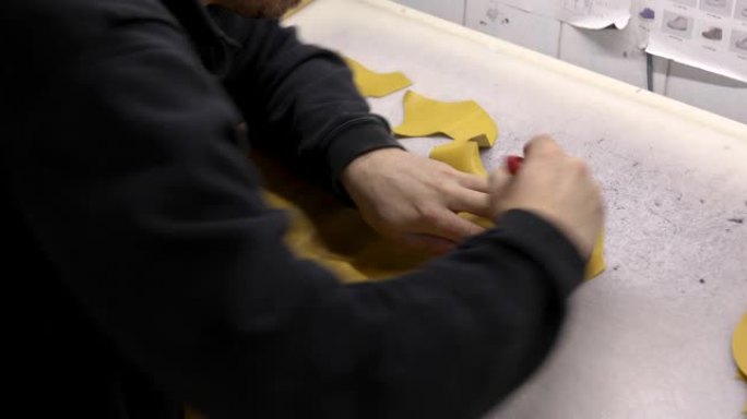 皮匠使用手术刀和金属图案从黄色皮革上切下儿童鞋的零件