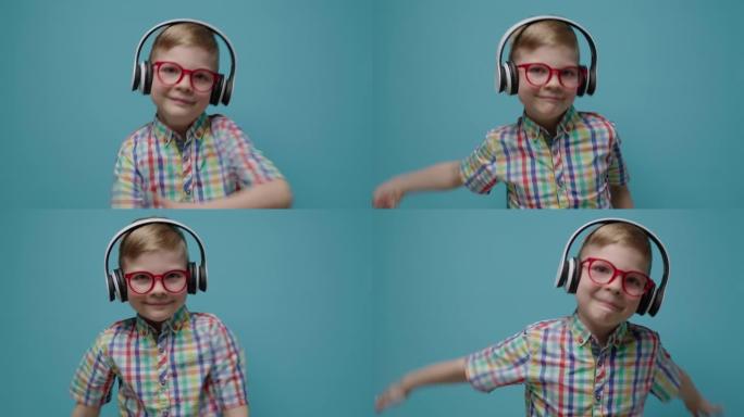 戴着眼镜和耳机的相当可爱的男生在慢动作的蓝色背景上跳舞。快乐的孩子看着相机跳舞。