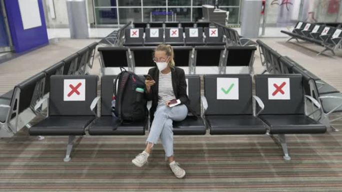 在等待登机时，女性游客在手机上上网，同时在新型冠状病毒肺炎大流行期间遵循所有规则作为新常态