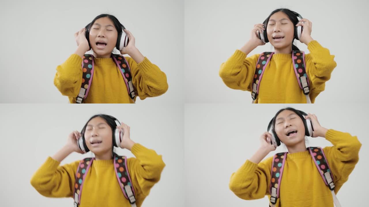 快乐的亚洲女学生使用无线耳机，在灰色背景下唱歌跳舞，生活方式理念。