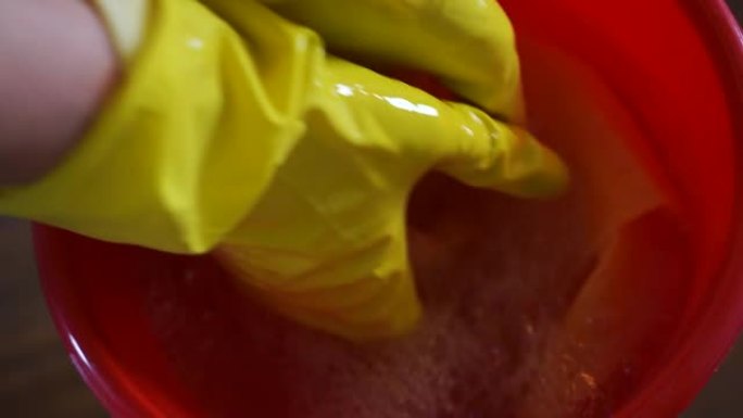 穿着黄色橡胶手套的女人在家用水桶弄湿抹布