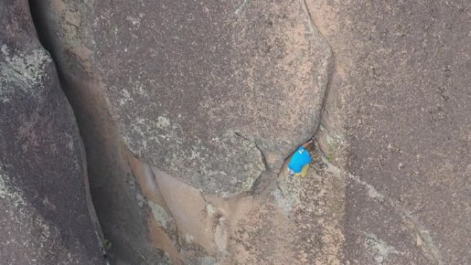 一个年轻勇敢的人在岩石裂缝上独自攀登的俯视图。