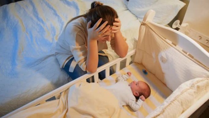 患有抑郁症的年轻疲惫的母亲晚上在婴儿床里看着她失眠的新生婴儿。产妇分娩后抑郁和不眠之夜。
