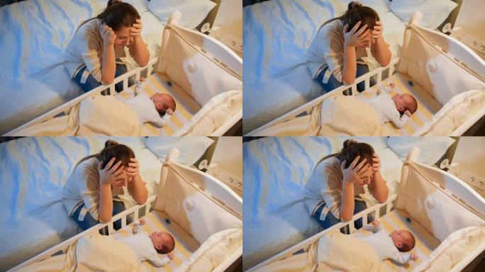 患有抑郁症的年轻疲惫的母亲晚上在婴儿床里看着她失眠的新生婴儿。产妇分娩后抑郁和不眠之夜。