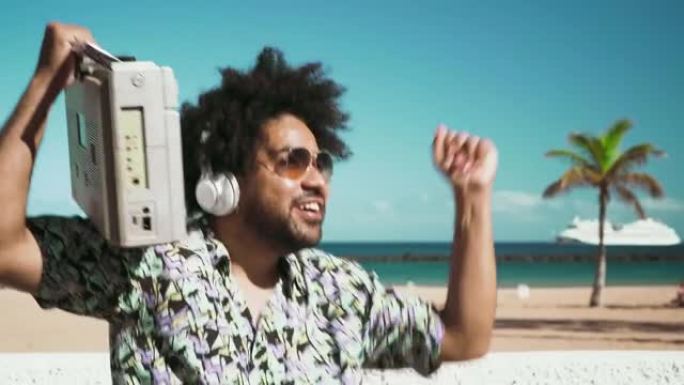 快乐的非洲裔男子在夏天在海滩上玩无线耳机和老式音箱听音乐