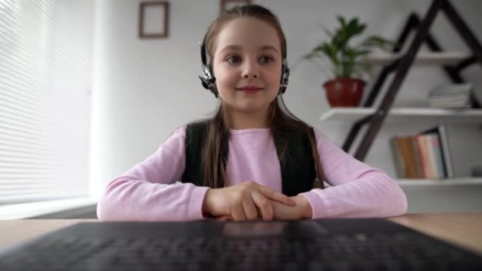 开朗的有动力的学生9岁的白人少年坐在笔记本电脑上的耳机里，向笔记本电脑的网络摄像头打招呼。在线教育视