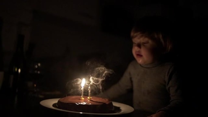 两岁的小孩在黑暗的慢动作中吹蜡烛